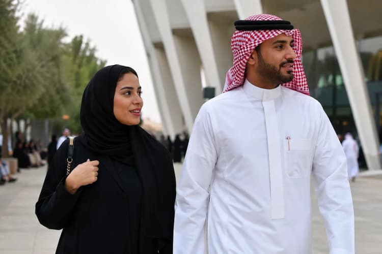 Man in white thobe with red ghutra headscarf, woman in flowing black abaya